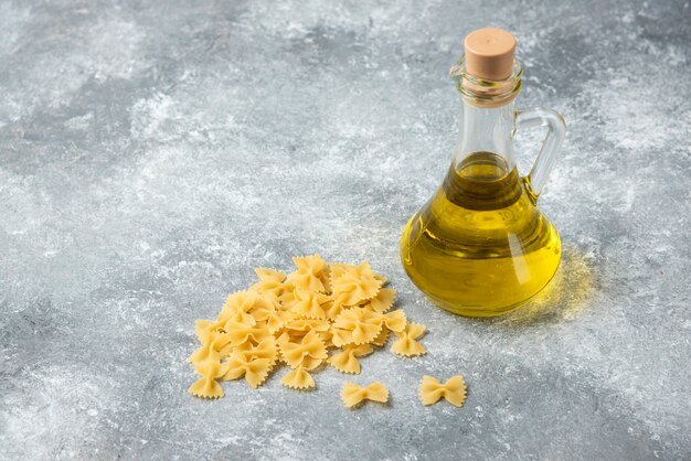 Pile of raw farfalle pasta with bottle of olive oil on marble background. 