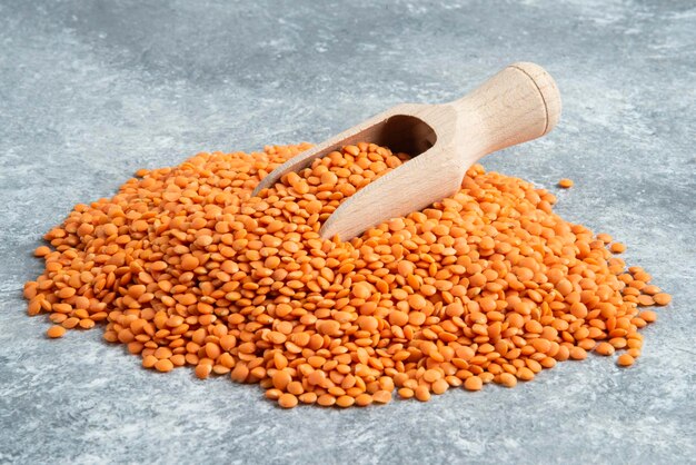 Pile of red lentils on marble surface with wooden spoon.