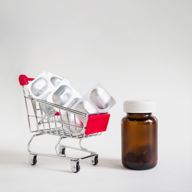 Free photo pill blisters in shopping cart with glass bottle on white background