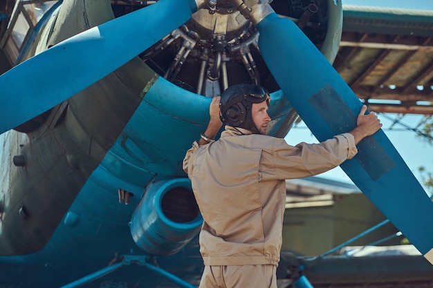 Free Photo pilot or mechanic in a full flight gear checks the propeller of his retro military aircraft before the flight.