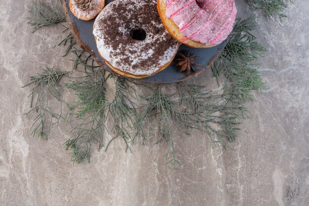 Pine leaves under a board with donuts on marble. 