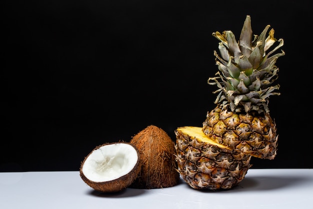 Pineapple and coconut cut in half on a table on a black