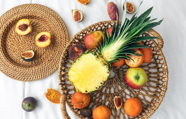 Pineapple and other exotic fruits in a basket on a white background top view