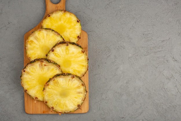 Pineapple slices lined juicy mellow fresh on brown wooden desk and grey background