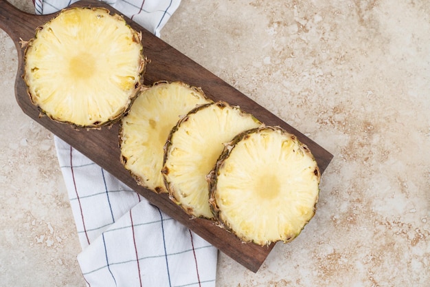 Pineapple slices on wooden board with towel on marble background.