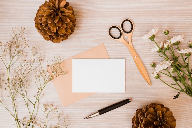 Pinecone; scissor; aster and baby's-breath flowers; fountain pen and blank card on wooden desk