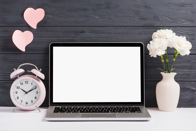 Pink alarm clock and flower vase on white desk against wooden wallpaper