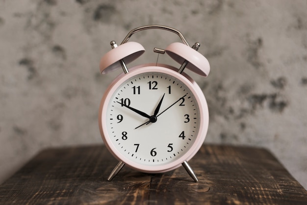 Pink alarm clock on wooden desk against weathered wall