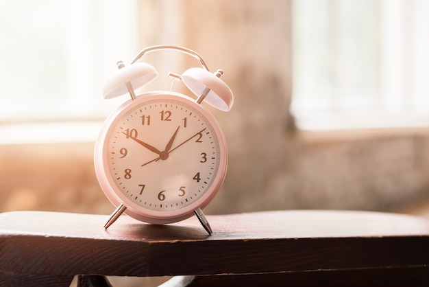 Pink alarm clock on wooden table in sunlight