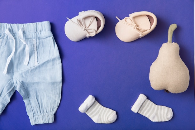 Free photo pink baby shoes; sock and baby's pant with stuffed pear on bright blue background