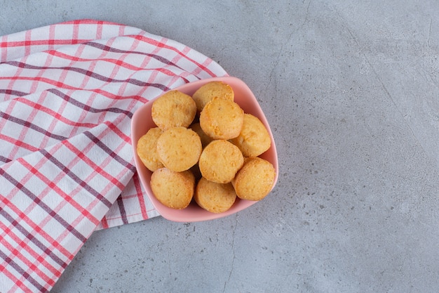 Pink bowl of mini sweet cakes on stone background.