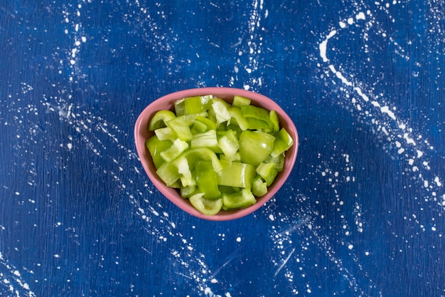 Free photo pink bowl of sliced green bell peppers on marble surface.