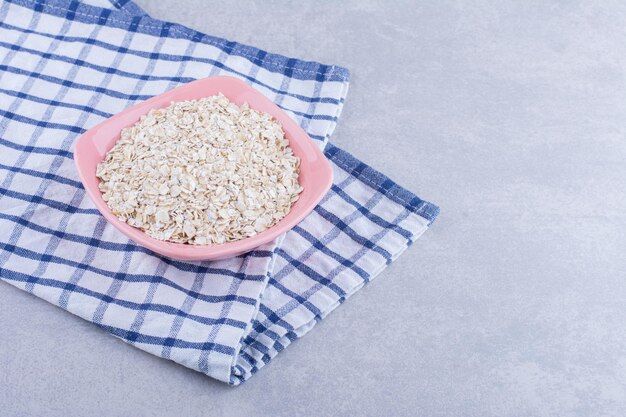 Pink bowl on a towel, filled with oat flakes, on marble surface