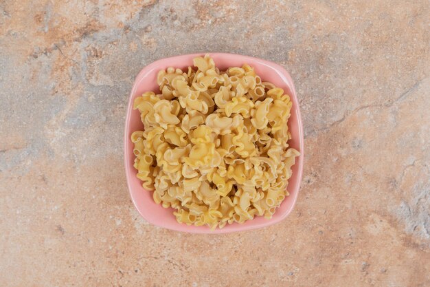 A pink bowl of unprepared macaroni on marble space. 