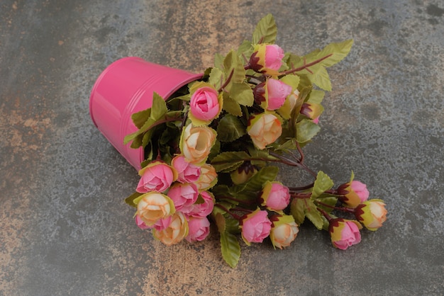 Free photo a pink bucket with bouquet of flowers on marble surface.