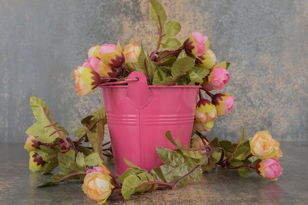 A pink bucket with bouquet of flowers on marble surface. 