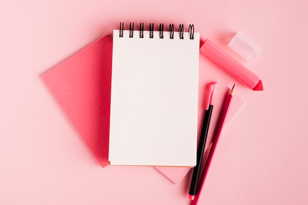 Pink composition with notepad and office supplies on colored surface