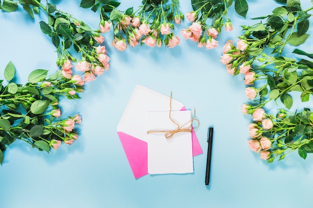 Free photo pink envelope; card; pen and roses flower decoration on blue background