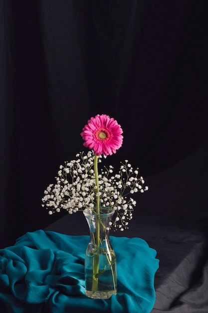 Free Photo pink flower with bloom twigs in vase near blue textile in obscurity