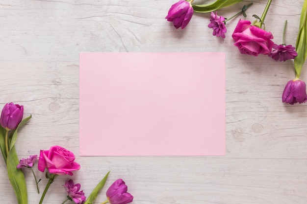 Free photo pink flowers with paper on wooden table