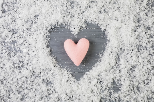 Pink heart between decorative snow on wooden desk