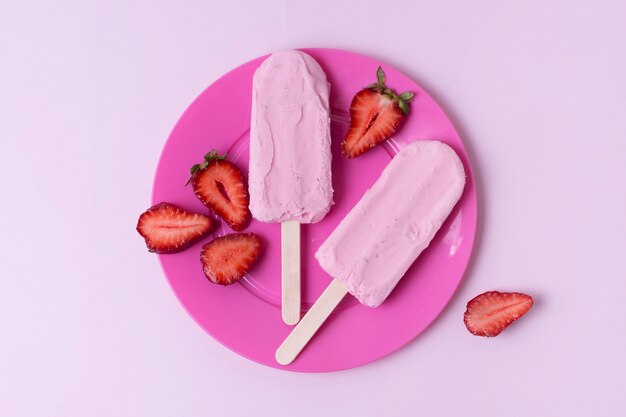 Pink ice cream on sticks and slices of strawberries