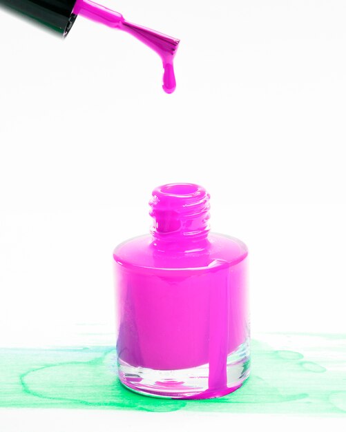 Pink nail polish dripping from brush in bottle on background