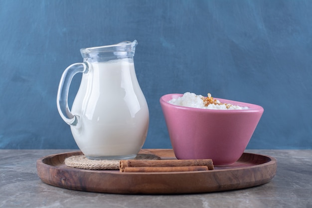 Free Photo a pink plate of healthy oatmeal porridge with a glass jug of milk and cinnamon sticks on a wooden board. 