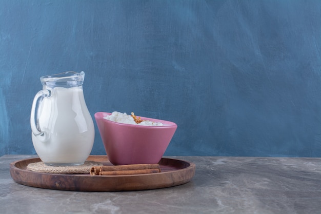 Free Photo a pink plate of healthy oatmeal porridge with a glass jug of milk and cinnamon sticks on a wooden board. 