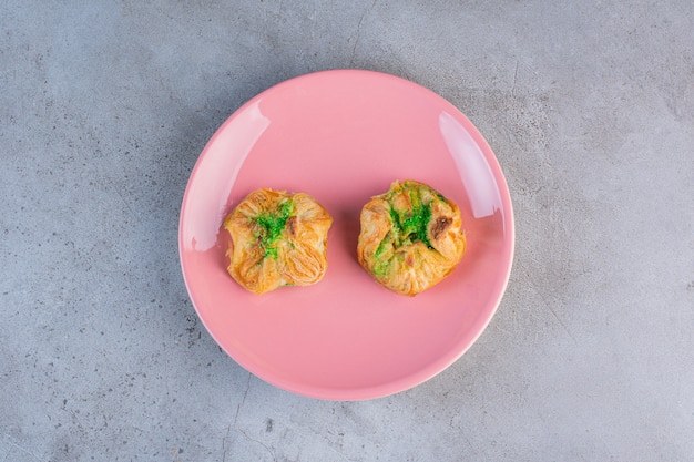 A pink plate with two delicious baklawas on gray