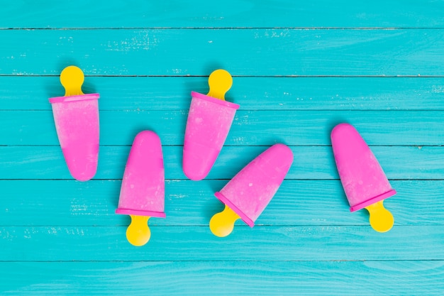 Free photo pink popsicle on yellow sticks on wooden surface