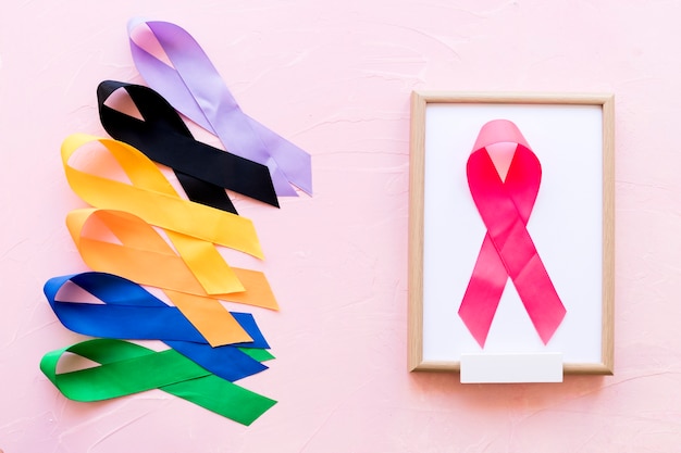 Pink ribbon on white wooden frame near the row of colorful awareness ribbon