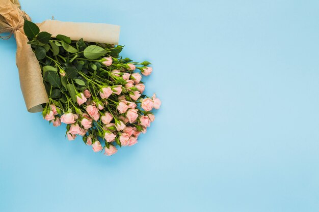 Pink rose bouquet wrapped in brown paper on blue background