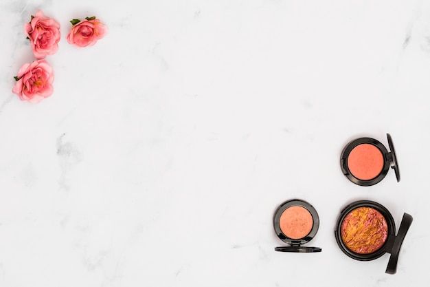 Pink rose flowers and compact powder on the corner of white backdrop