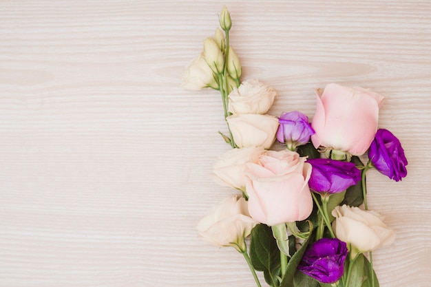 Free photo pink roses and purple eustoma flowers on wooden desk