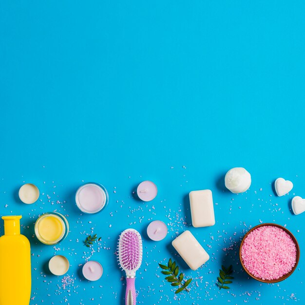 Pink salt; soap; cream and shampoo with different types of candles on blue backdrop