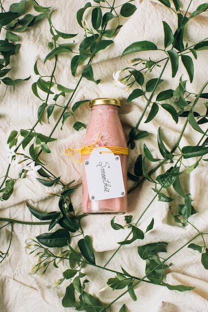 Free photo pink smoothie in a bottle next to leaves