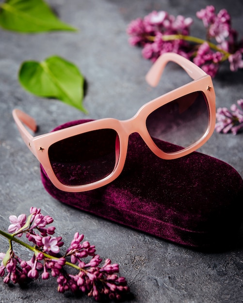 Free photo pink sunglasses around beatiful flowers on the grey surface