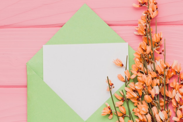 Free photo pink surface with blank paper and floral decoration