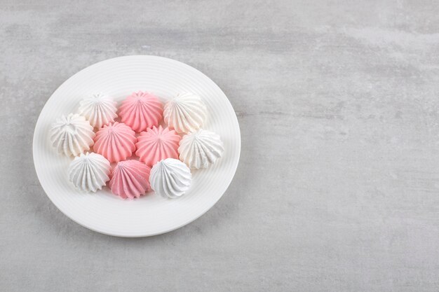 Pink and white meringue on a plate, on the marble table. 