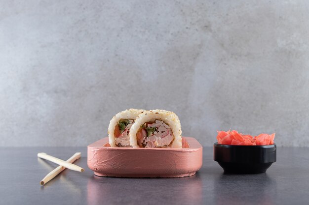 Pink wooden board of delicious sushi roll placed on stone background . 