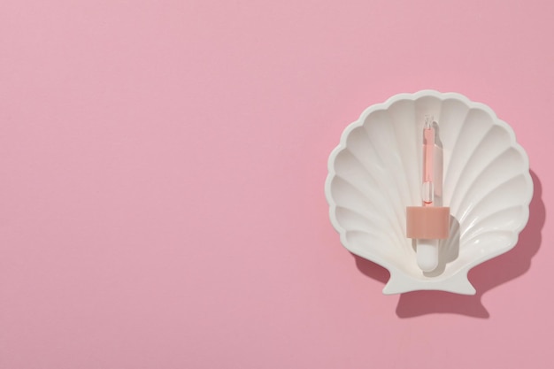 Free Photo pipette with serum on seashell on pink background space for text