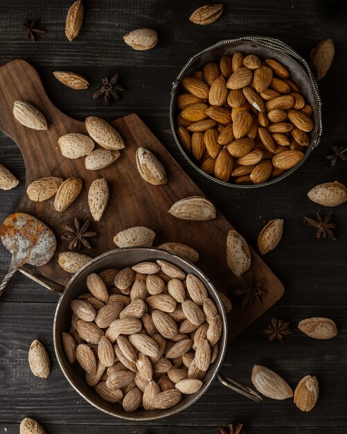 Pistachios and almonds inside black bowles and on a wooden board.