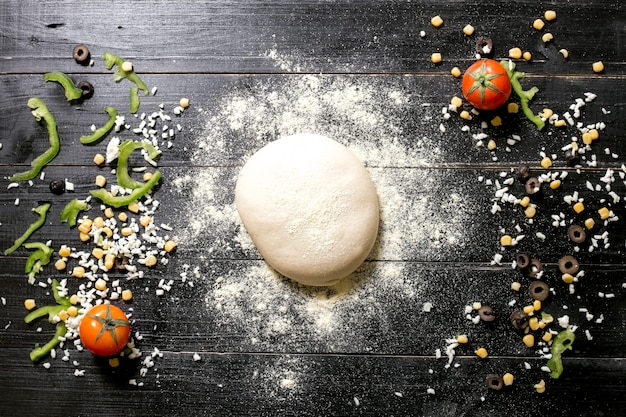 Free photo pizza dough sprinkled with flour placed next to cheese sprinkles olive corn tomato bell pepper