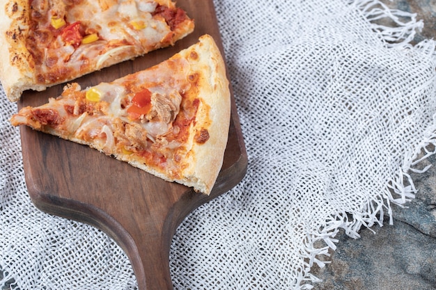 Free photo pizza slices with melted cheese on the top on a wooden board on a piece of white burlap