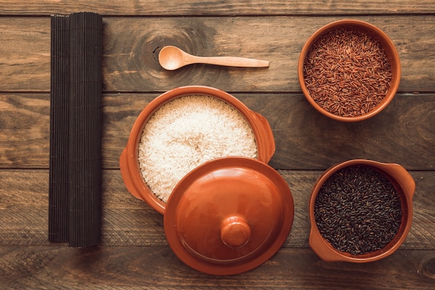 Place mat with uncooked rice in different bowls on wooden table