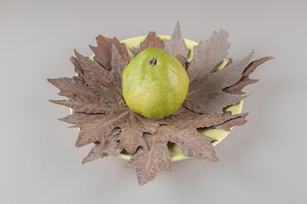 Free photo plane tree leaves under a single pear on a platter on marble