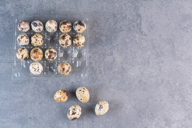 Plastic container of raw quail eggs on stone table.