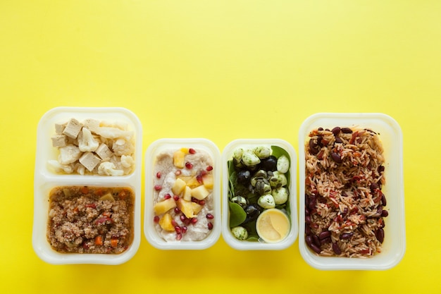 Plastic containers with delicious food over yellow surface