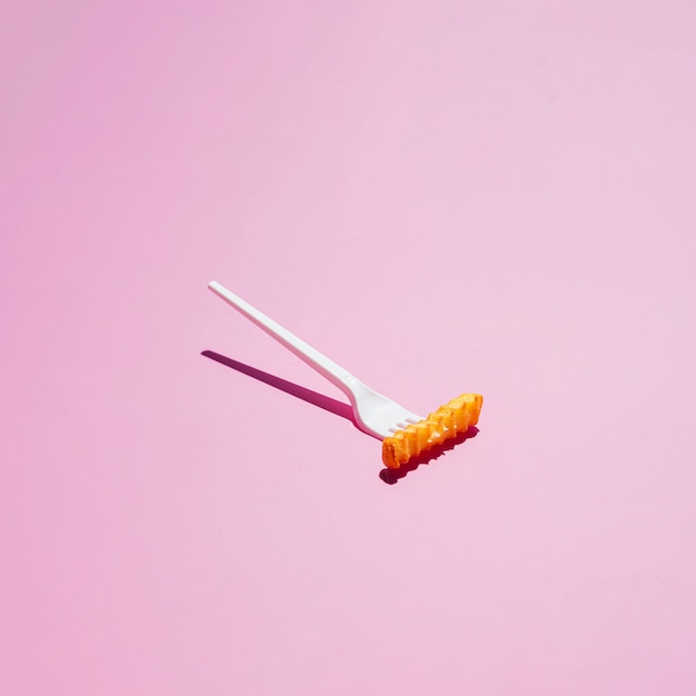 Free photo plastic fork and french fries on pink background